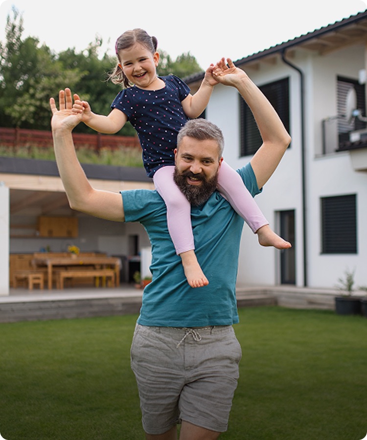 A father with his daughter on his shoulders outside their home